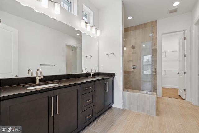 bathroom with a sink, a walk in closet, double vanity, and a tile shower