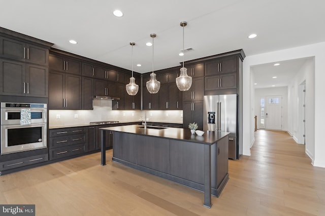 kitchen with dark countertops, dark brown cabinets, appliances with stainless steel finishes, light wood-style floors, and a sink