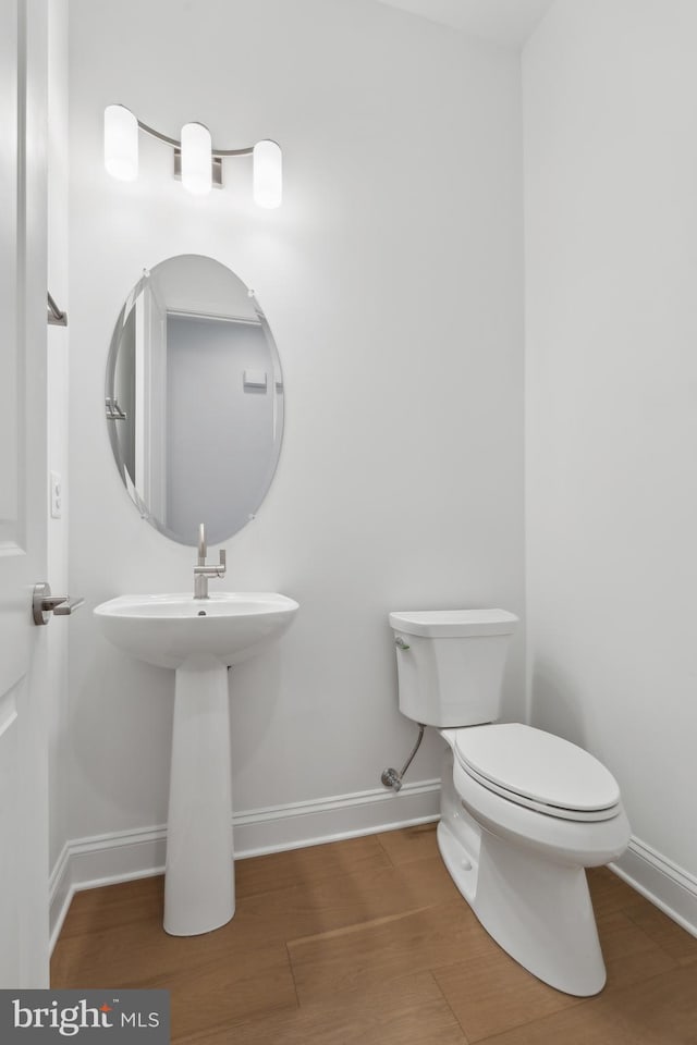 half bath featuring a sink, toilet, baseboards, and wood finished floors