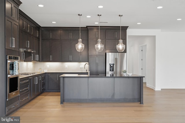 kitchen featuring dark brown cabinetry, light wood-style flooring, a center island with sink, and appliances with stainless steel finishes