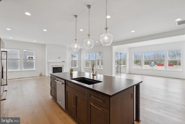 kitchen featuring a sink, dishwasher, a glass covered fireplace, dark countertops, and open floor plan