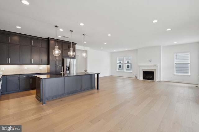 kitchen with a center island with sink, stainless steel fridge with ice dispenser, a sink, dark brown cabinets, and light wood-type flooring