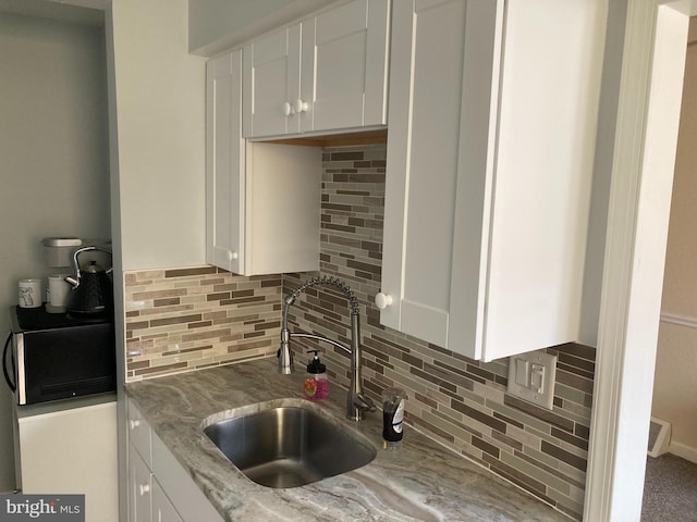 kitchen featuring white cabinets, light stone counters, tasteful backsplash, and a sink