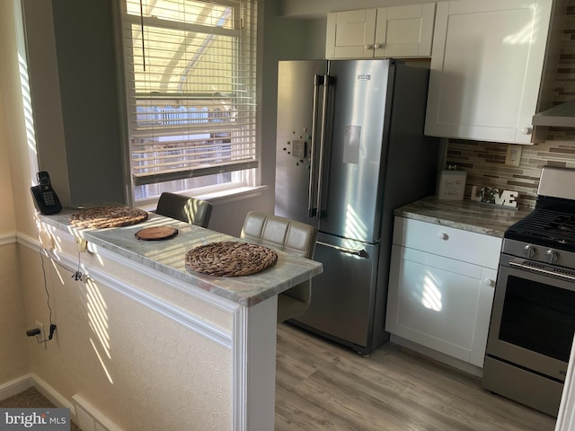 kitchen with stainless steel appliances, white cabinets, light wood-style floors, wall chimney range hood, and backsplash