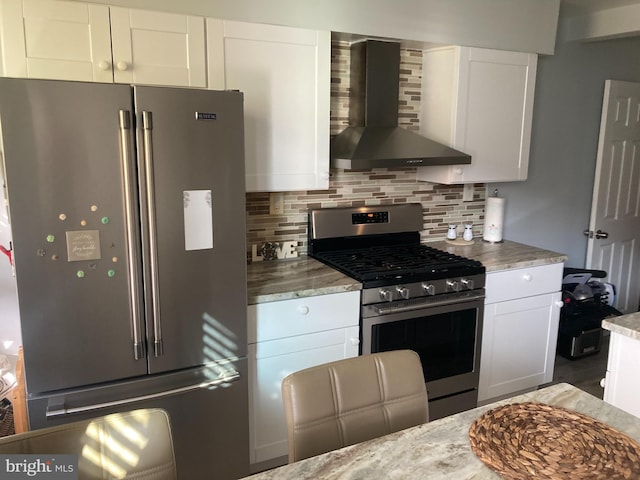 kitchen featuring decorative backsplash, white cabinetry, stainless steel appliances, and wall chimney exhaust hood