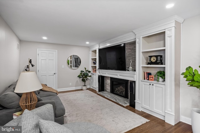 living room with a high end fireplace, dark wood-type flooring, baseboards, built in features, and recessed lighting