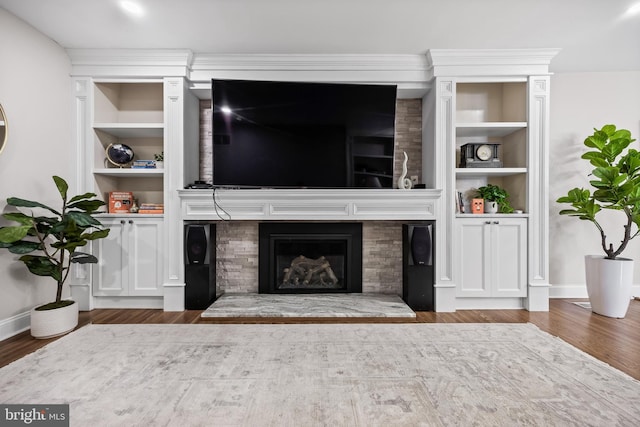 living room with built in shelves, a large fireplace, baseboards, and wood finished floors