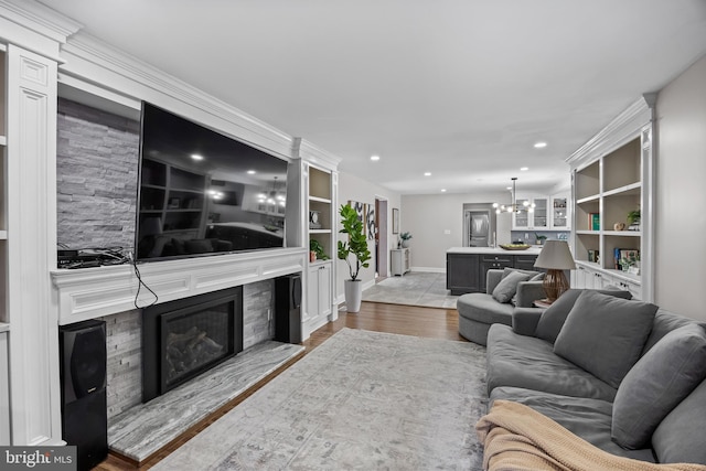 living room with a chandelier, built in features, recessed lighting, wood finished floors, and a glass covered fireplace