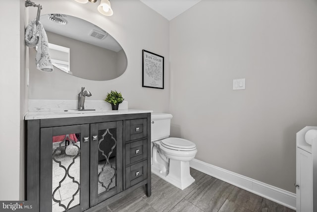 bathroom featuring visible vents, toilet, wood finished floors, baseboards, and vanity