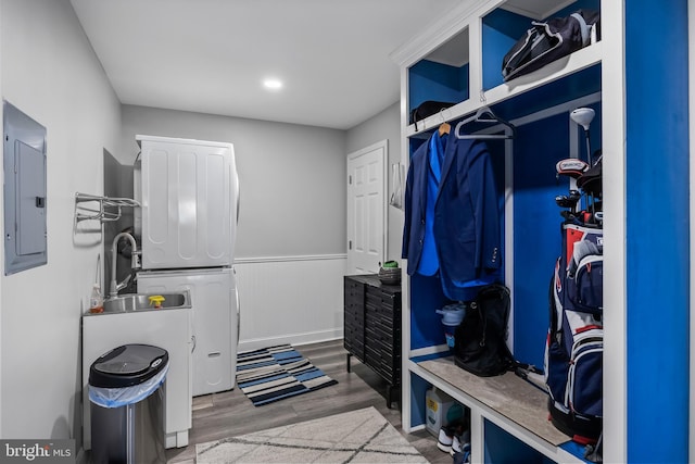 laundry room with electric panel, wood finished floors, stacked washing maching and dryer, wainscoting, and laundry area