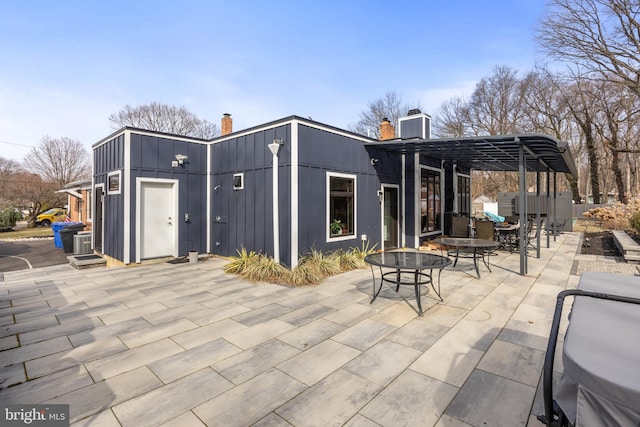 back of house with outdoor dining space, central AC, board and batten siding, a chimney, and a patio area