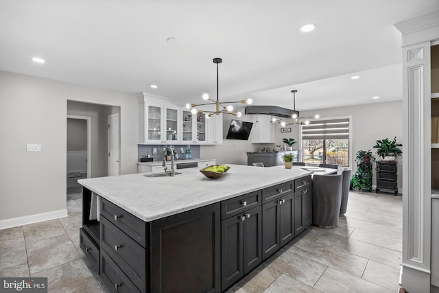 kitchen featuring an inviting chandelier, an island with sink, a sink, white cabinets, and glass insert cabinets