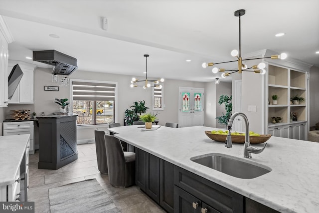 kitchen featuring white cabinetry, an inviting chandelier, light stone counters, and a sink