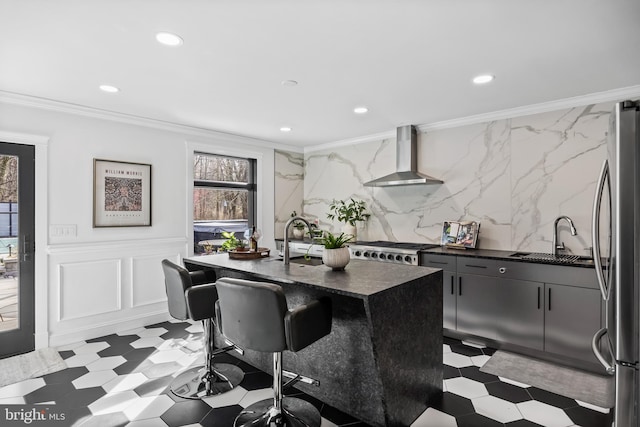 kitchen with ornamental molding, freestanding refrigerator, wall chimney range hood, and a sink