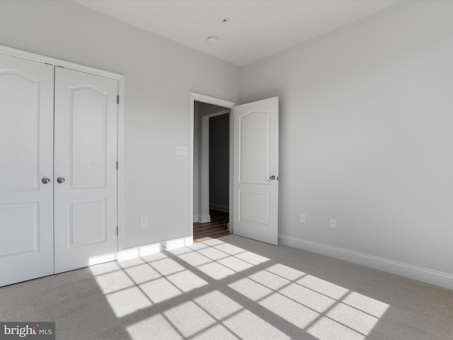 unfurnished bedroom featuring a closet, light colored carpet, and baseboards