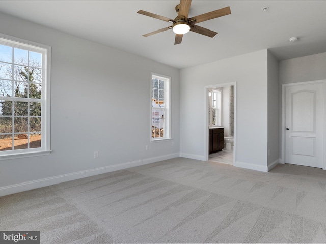 unfurnished bedroom with multiple windows, light carpet, baseboards, and connected bathroom