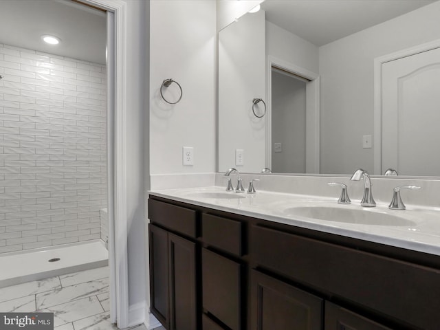 full bath featuring double vanity, marble finish floor, a tile shower, and a sink