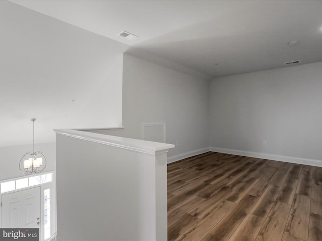 empty room with baseboards, wood finished floors, visible vents, and a chandelier