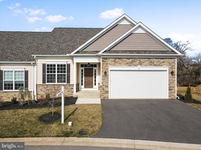 craftsman-style house featuring a front lawn, driveway, stone siding, an attached garage, and a shingled roof