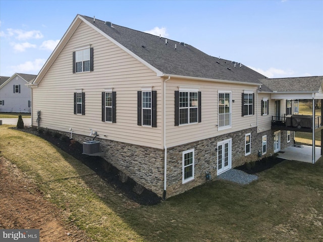 rear view of house featuring a yard, central AC unit, stone siding, and a shingled roof