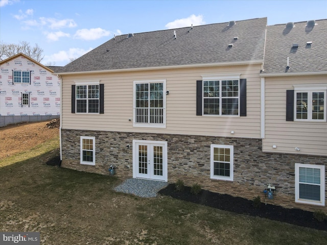 back of property featuring french doors, stone siding, a yard, and roof with shingles