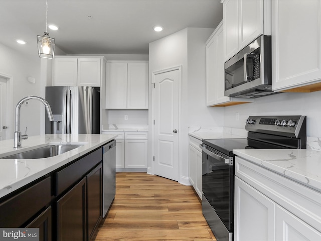 kitchen featuring light wood finished floors, white cabinets, appliances with stainless steel finishes, and a sink