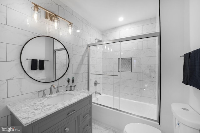 bathroom featuring toilet, vanity, combined bath / shower with glass door, marble finish floor, and tile walls