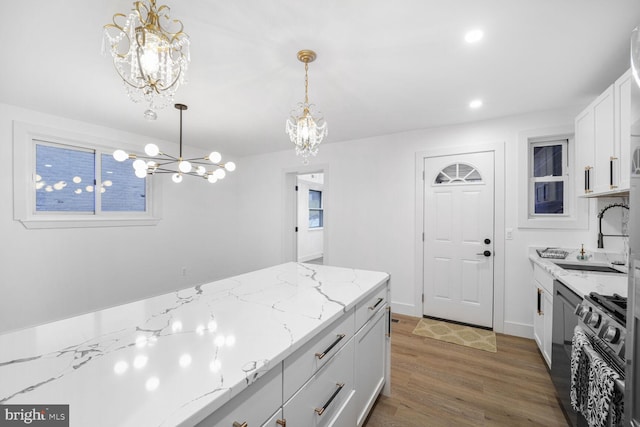 kitchen with a notable chandelier, a sink, wood finished floors, stainless steel range with gas cooktop, and hanging light fixtures