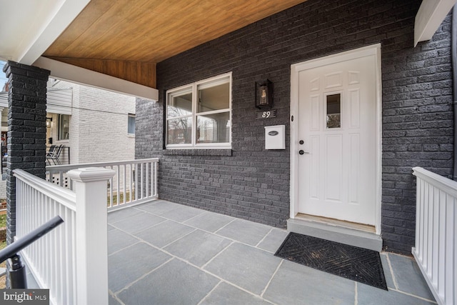 doorway to property featuring brick siding and a porch