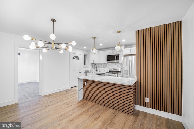 kitchen featuring backsplash, white cabinetry, stainless steel appliances, light wood-style floors, and a peninsula