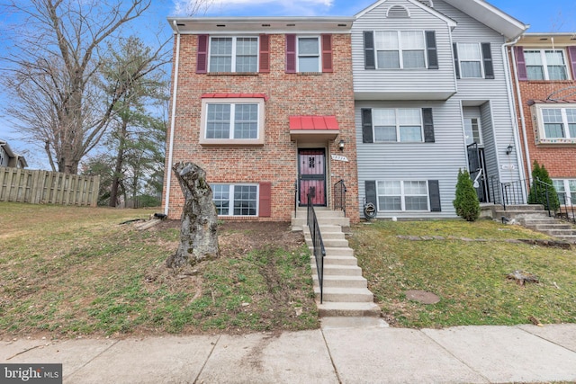 multi unit property with brick siding, a front yard, and fence