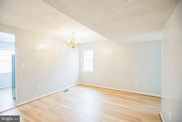 empty room featuring a notable chandelier, wood finished floors, visible vents, and a textured ceiling