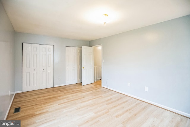 unfurnished bedroom with light wood-style flooring, baseboards, visible vents, and two closets