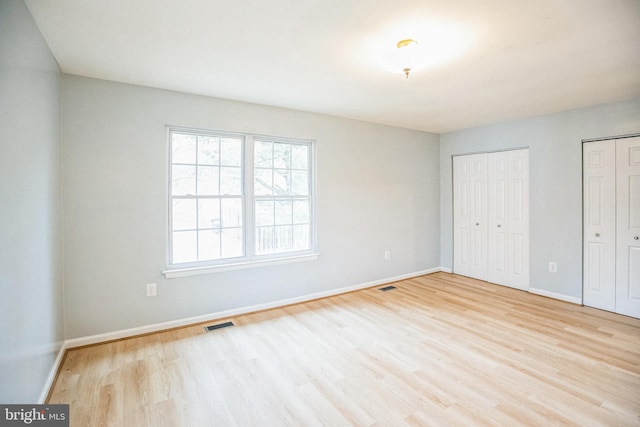 unfurnished bedroom with visible vents, wood finished floors, baseboards, and two closets