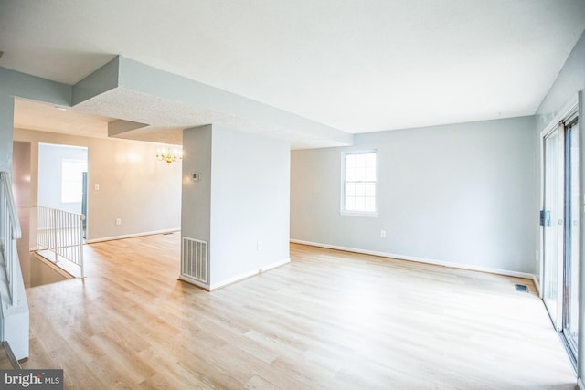 unfurnished room featuring a notable chandelier, light wood-style floors, visible vents, and baseboards