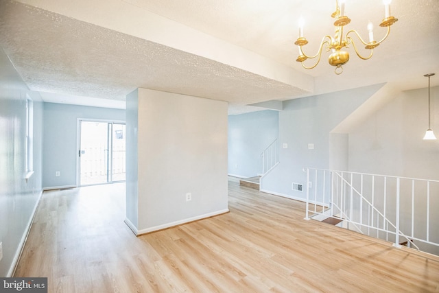 spare room with visible vents, a textured ceiling, an inviting chandelier, and wood finished floors