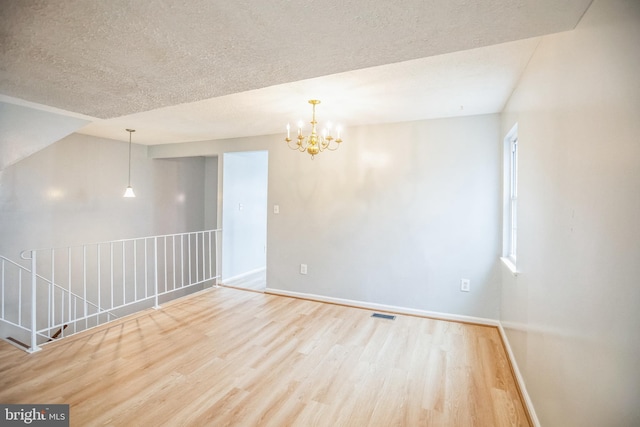 empty room with visible vents, baseboards, an inviting chandelier, wood finished floors, and a textured ceiling