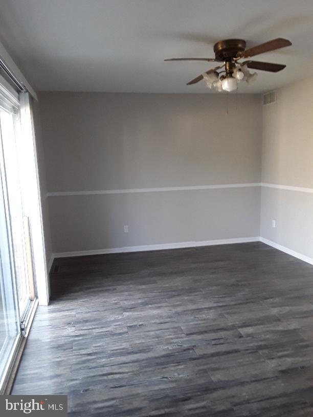 unfurnished room with dark wood-style floors, a ceiling fan, visible vents, and baseboards