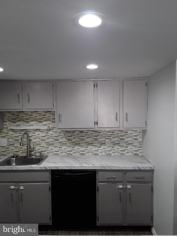 kitchen with decorative backsplash, gray cabinets, black dishwasher, and a sink