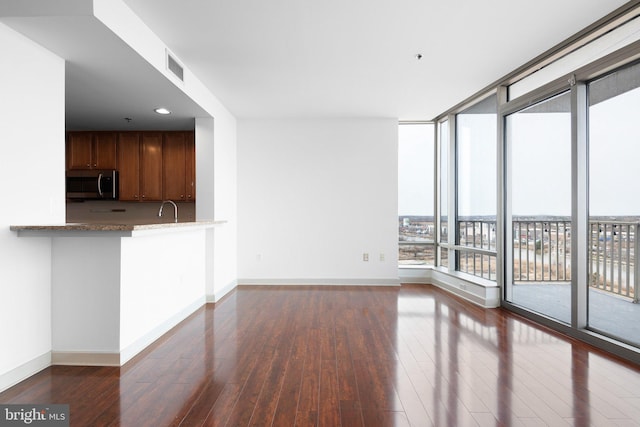 unfurnished living room featuring visible vents, baseboards, a sink, dark wood-type flooring, and floor to ceiling windows