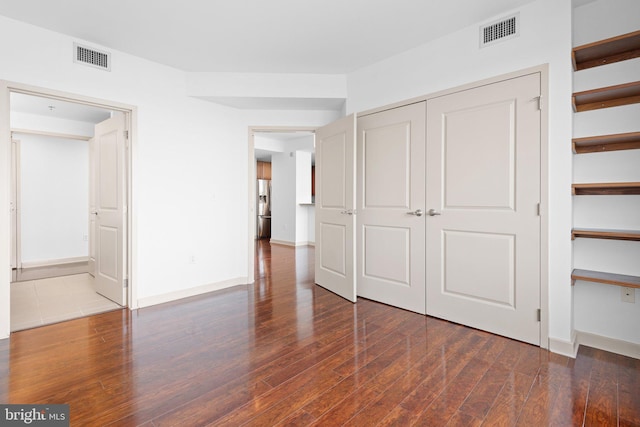 unfurnished bedroom with visible vents, stainless steel fridge, baseboards, and hardwood / wood-style floors