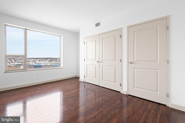 unfurnished bedroom with a closet, visible vents, baseboards, and wood finished floors