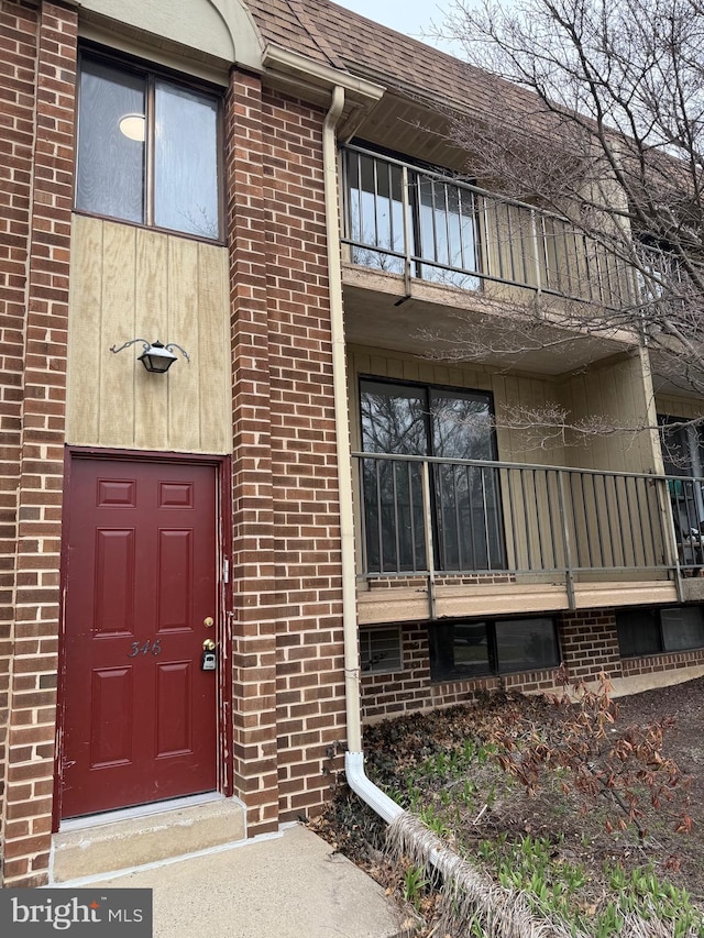 view of exterior entry featuring brick siding, a balcony, and roof with shingles