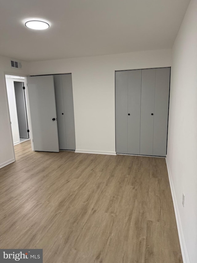 unfurnished bedroom featuring visible vents, light wood-type flooring, two closets, and baseboards