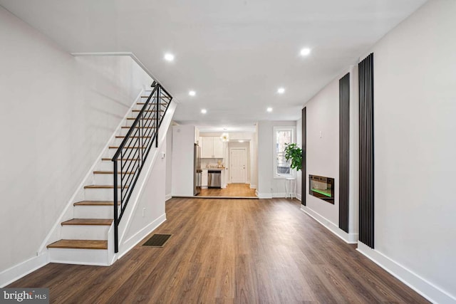 unfurnished living room featuring wood finished floors, visible vents, baseboards, recessed lighting, and stairs