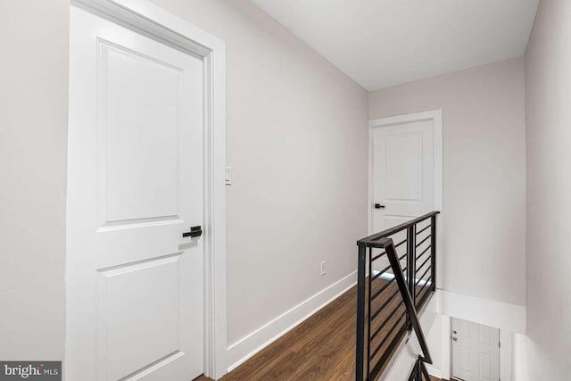 hallway with an upstairs landing, baseboards, and dark wood-style flooring