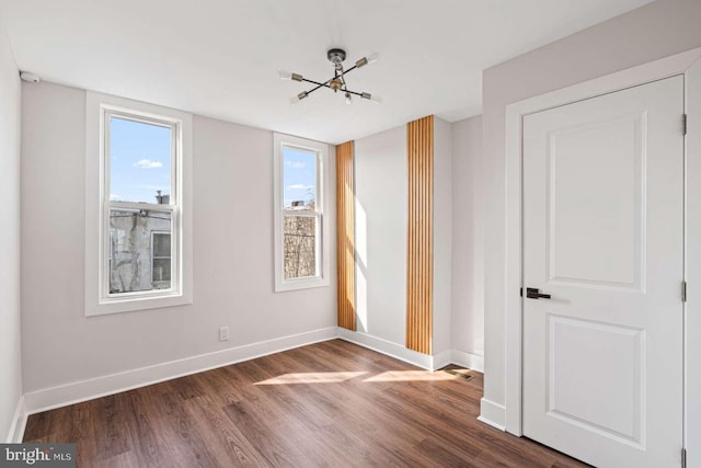 unfurnished room featuring a wealth of natural light, a notable chandelier, dark wood finished floors, and baseboards