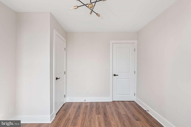 unfurnished room featuring baseboards, a notable chandelier, and wood finished floors