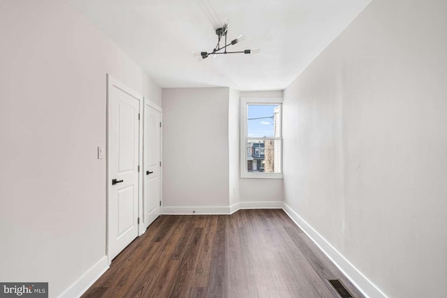 unfurnished room with a notable chandelier, visible vents, baseboards, and dark wood-style flooring