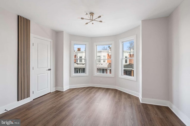 spare room featuring a chandelier, dark wood-style floors, and baseboards